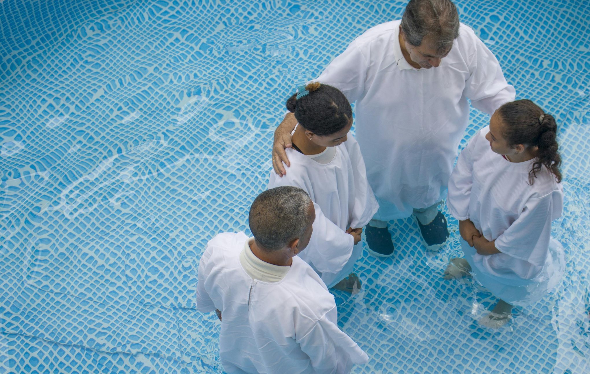 Aerial view of a baptism ceremony in a pool with a diverse group of people in white robes.